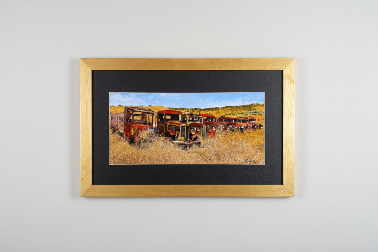 A framed vertical art print depicting a row of red farm tractors in a golden field under a blue sky, mounted on a textured white wall.